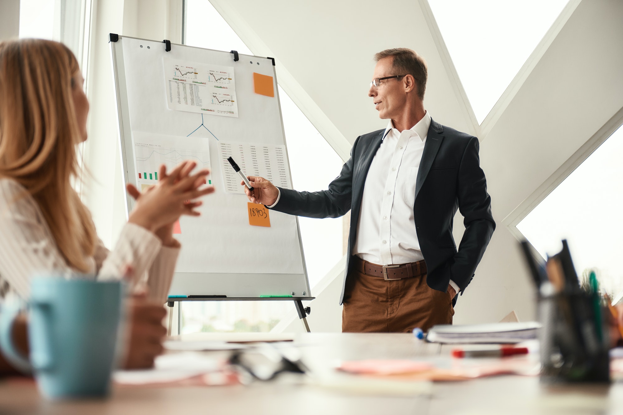 Look here. Mature businessman standing near whiteboard and explaining something to his young